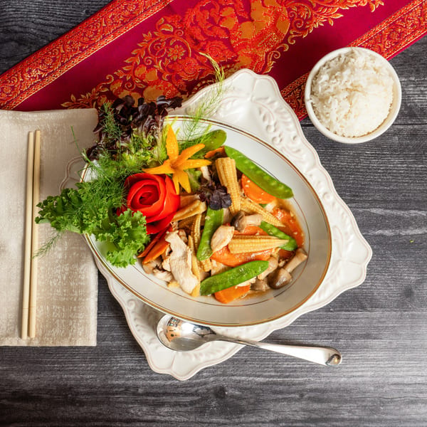 Stir-fried chicken with baby corn, snow peas, carrots, and mushrooms, served with rice.