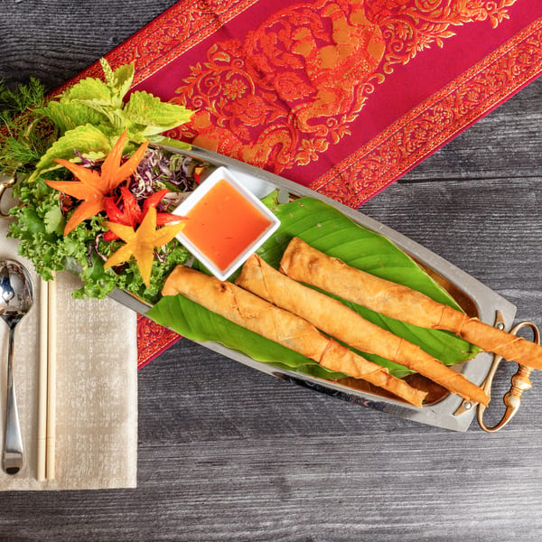 Crispy spring rolls with sweet chili sauce, fresh greens, and carved vegetables on a silver tray.