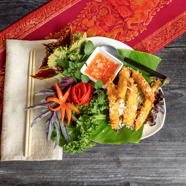 Crispy fried shrimp with sweet chili sauce, garnished with fresh herbs and carved vegetables.