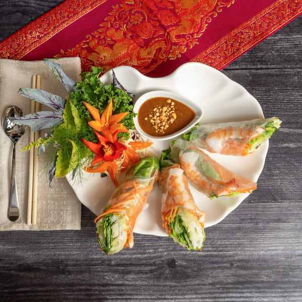 Shrimp spring rolls with peanut sauce, garnished with lettuce and carved carrots on a white plate.
