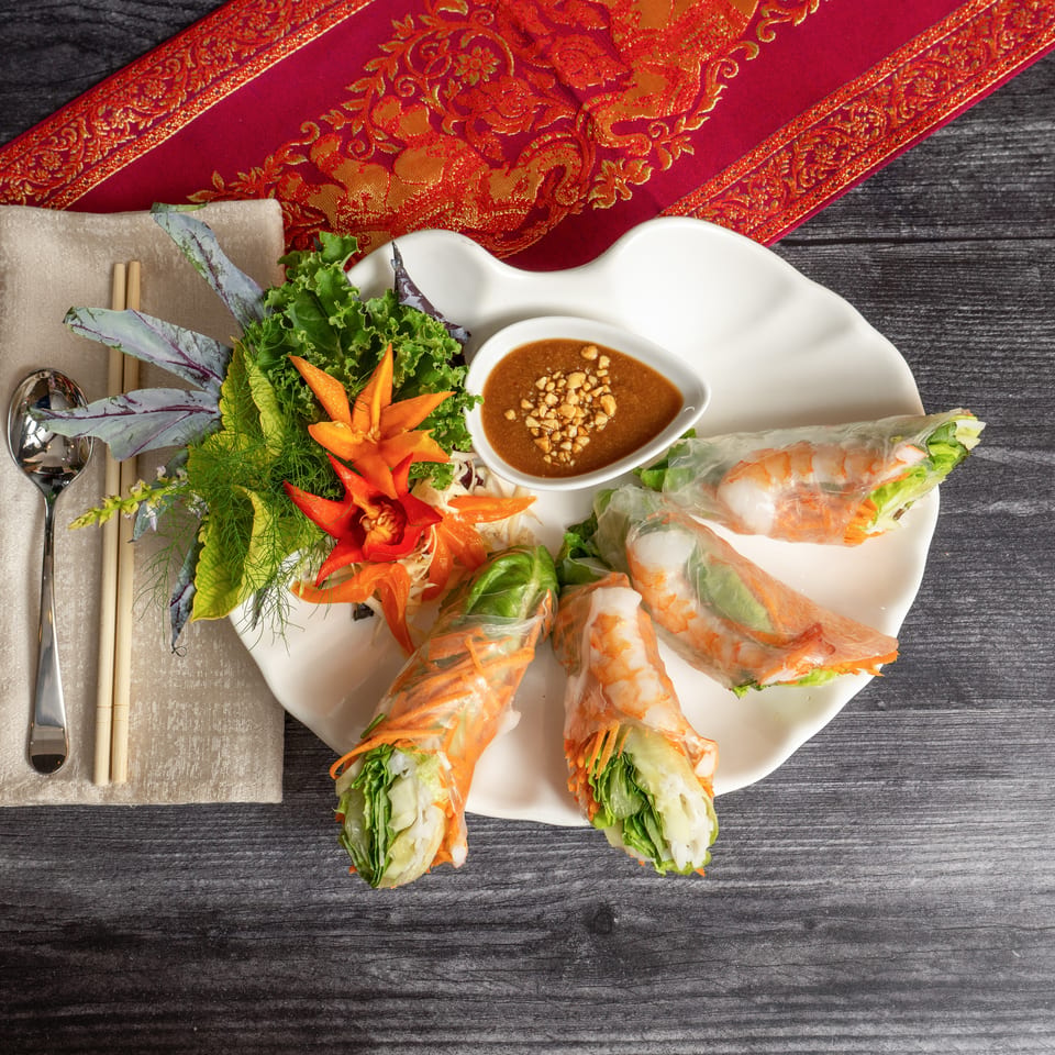 Shrimp spring rolls with peanut sauce, garnished with lettuce and carved carrots on a white plate.