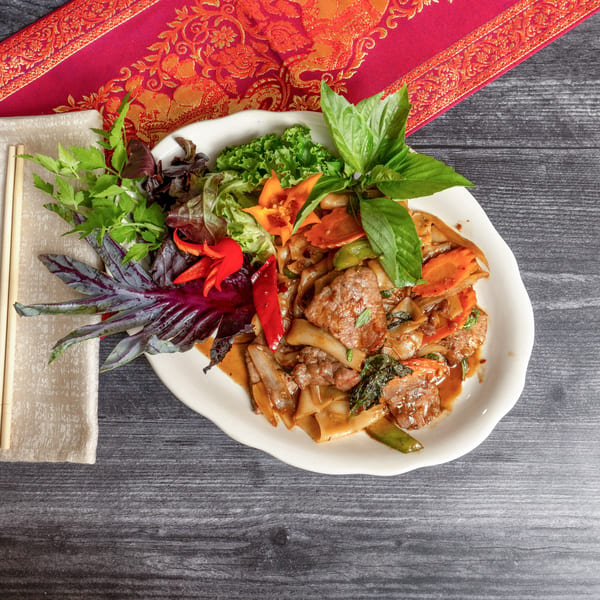 Thai Drunken Noodles with beef, vegetables, and herbs, served on a white plate with chopsticks.