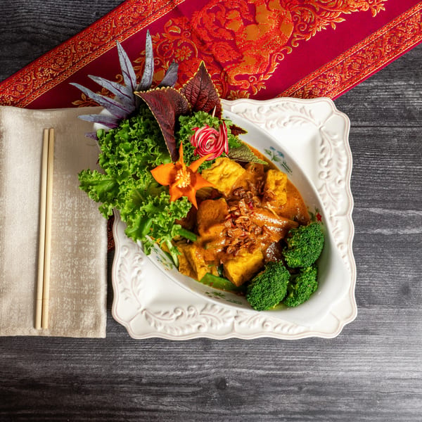 Curry dish with tofu, broccoli, and lettuce, garnished with fried onions, on a decorative plate.