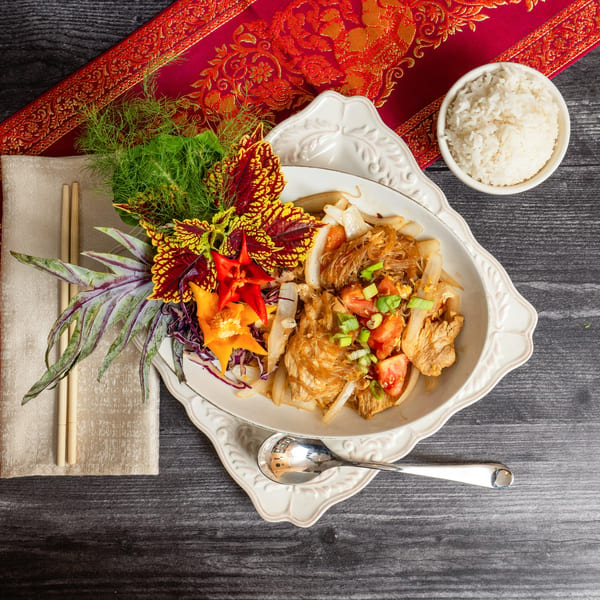 Glass noodle stir-fry with chicken, onions, tomatoes, and scallions, served with rice and chopsticks.